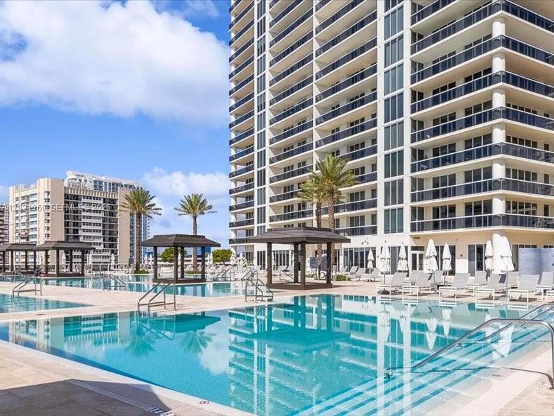 A large swimming pool sits in front of a tall residential building with balconies — 1800 S Ocean Dr # 3101, Hallandale Beach FL 33009, HALLANDALE BEACH, FL