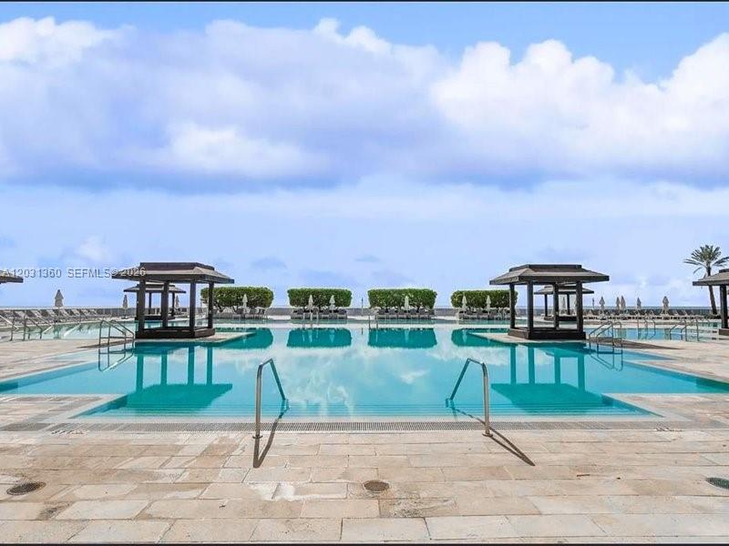 A swimming pool with two cabanas overlooks the ocean under a cloudy sky — 1800 S Ocean Dr # 3101, Hallandale Beach FL 33009, HALLANDALE BEACH, FL