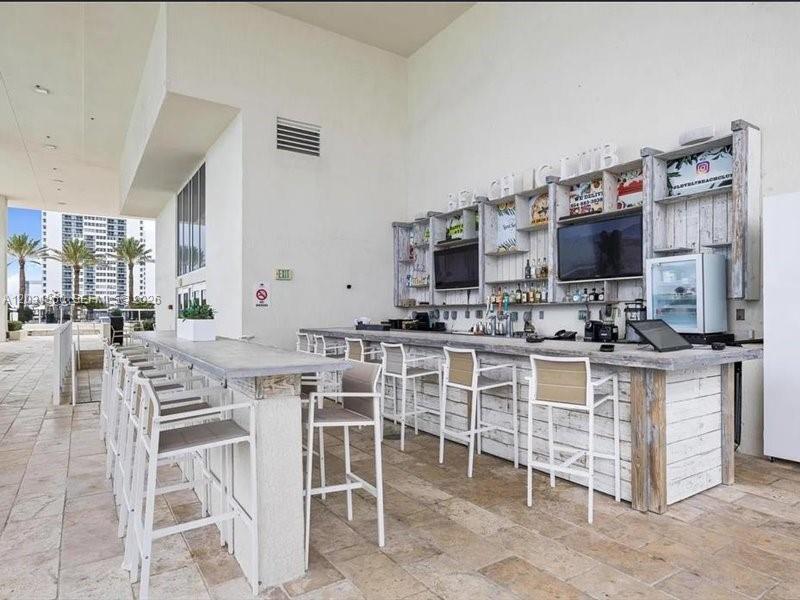An outdoor bar area features a rustic wooden counter, stools, and shelving with televisions — 1800 S Ocean Dr # 3101, Hallandale Beach FL 33009, HALLANDALE BEACH, FL