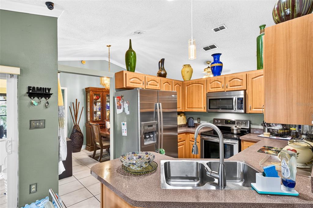 A kitchen with wood cabinets, stainless steel appliances, and a peninsula sink overlooks a dining area — 6616 CORAL COVE DRIVE, ORLANDO, FL