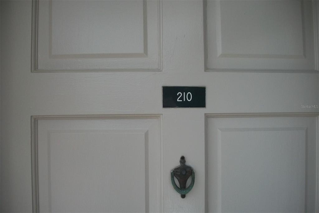 A white paneled door features a black room number sign labeled 210 and a door knocker — 10540 77TH TERRACE UNIT 210, SEMINOLE, FL