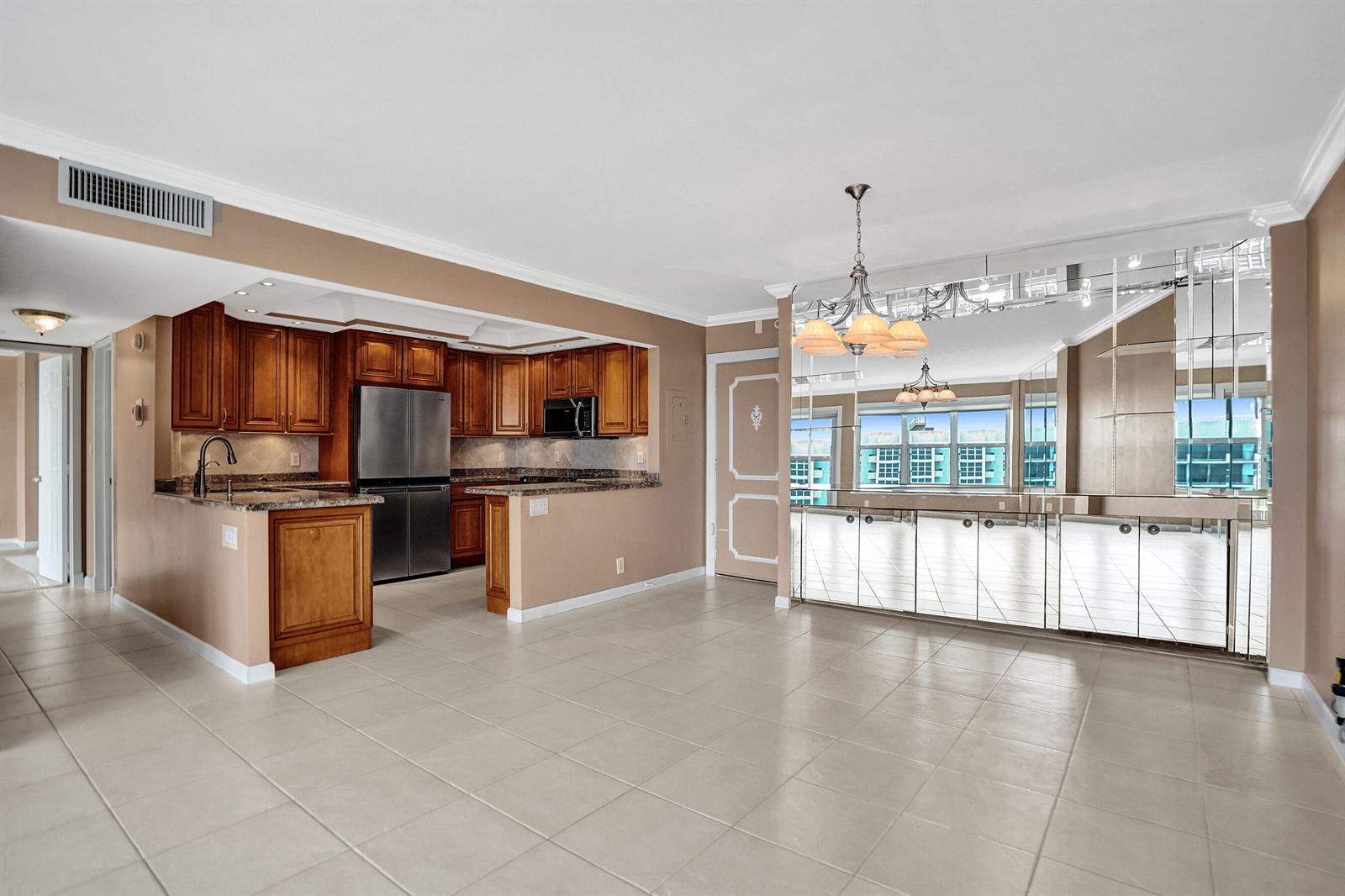 A kitchen with wood cabinets and granite countertops opens to a dining area with mirrors — 405 N Ocean Boulevard # 1803, Pompano Beach FL 33062, POMPANO BEACH, FL