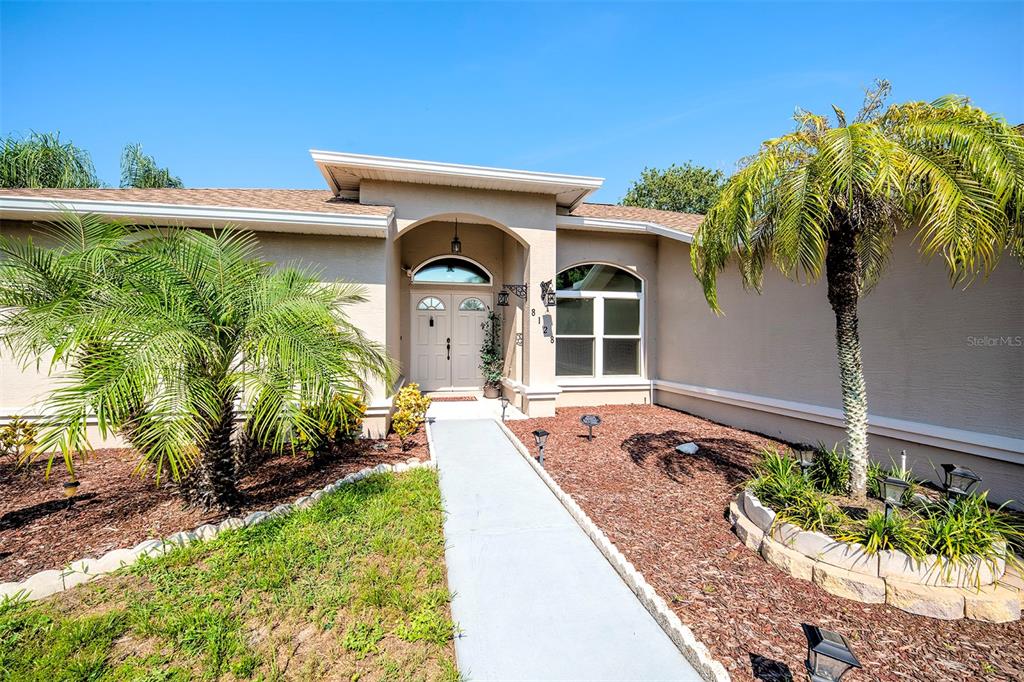 A single-story house exterior features a beige stucco facade, arched entryway, and a palm tree — 8128 GOLDEN BEAR LOOP, PORT RICHEY, FL