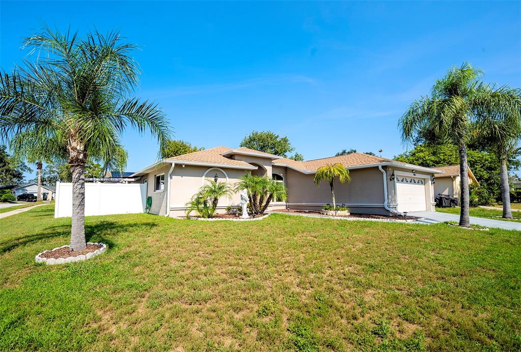 A single-story tan house with a garage and palm trees sits on a grassy lawn — 8128 GOLDEN BEAR LOOP, PORT RICHEY, FL