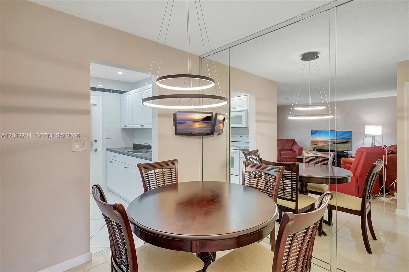 A dining area features a round wooden table, modern pendant lighting, and mirrored wall panels — 17001 NE 13th ave # 306, Miami FL 33162, MIAMI, FL