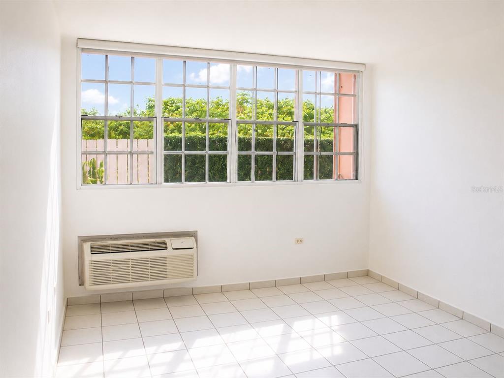 A bright, empty room features white tile flooring, plain white walls, and a large window — BOULEVARD DEL RIO II, GUAYNABO, PR