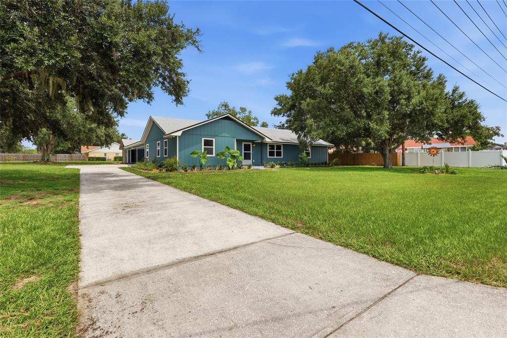 A teal single-story house with a concrete driveway and large trees in the front yard — 6028 YARBOROUGH LANE, LAKELAND, FL