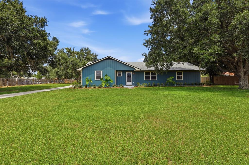 A blue, single-story house with a gabled roof sits on a large, grassy lot — 6028 YARBOROUGH LANE, LAKELAND, FL