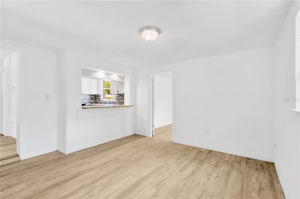 An empty room with light wood-look flooring and a pass-through window to the kitchen — 1940 N BETTY LANE, CLEARWATER, FL