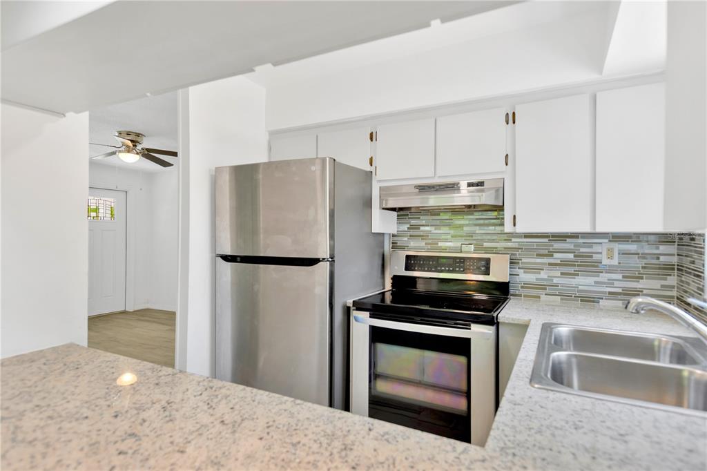 A kitchen features stainless steel appliances, white cabinets, a tiled backsplash, and granite countertops — 1940 N BETTY LANE, CLEARWATER, FL