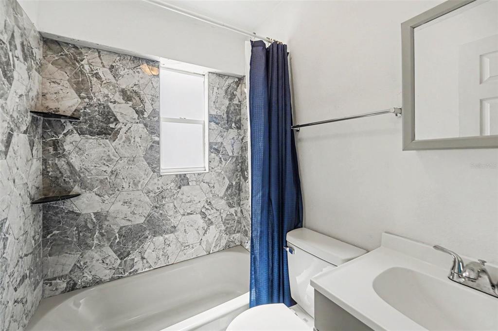 A bathroom features a bathtub with gray marble-patterned hexagonal tile walls and a blue curtain — 1940 N BETTY LANE, CLEARWATER, FL