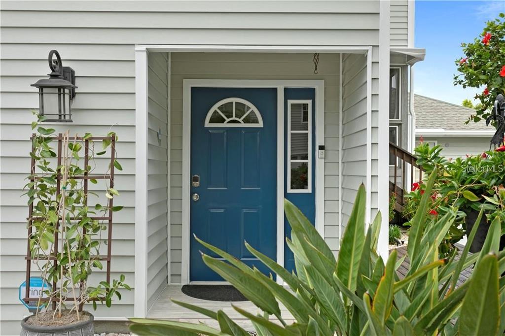 A blue front door with a sidelight window sits under a covered entryway with siding — 11722 CURRIE LANE UNIT J1, LARGO, FL