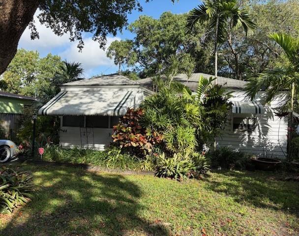 A white house with a striped awning is surrounded by lush tropical landscaping and trees — 44 SW 5th Street, Dania Beach FL 33004, DANIA BEACH, FL