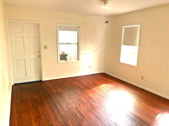 An empty room features hardwood floors, two windows, and a white door — 44 SW 5th Street, Dania Beach FL 33004, DANIA BEACH, FL