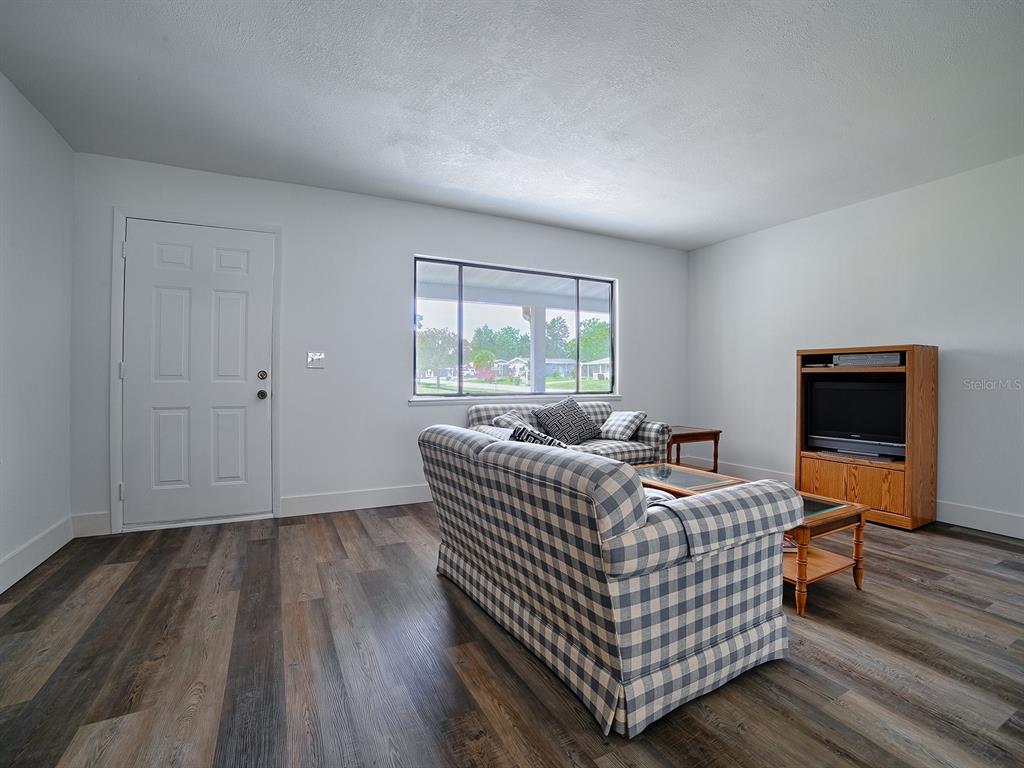 A living room features wood-look flooring, a plaid sofa, and a wooden television console — 9115 SW 102ND LANE, OCALA, FL