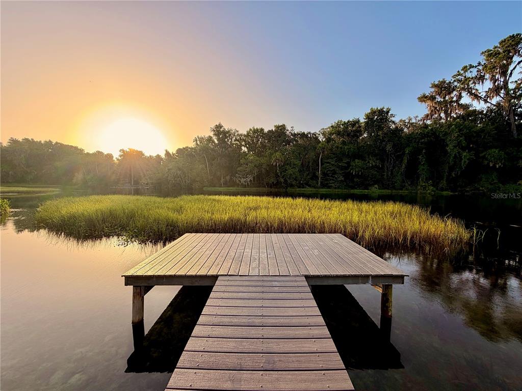 A wooden dock extends into a calm lake with tall grasses at sunset — 9275 SW 186TH TERRACE, DUNNELLON, FL