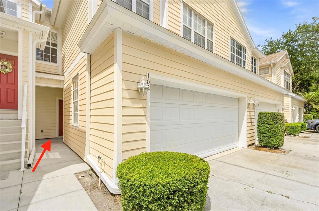A yellow-sided townhouse exterior features a white garage door, a front entrance, and landscaping — 6216 ROSEFINCH COURT UNIT 102, LAKEWOOD RANCH, FL