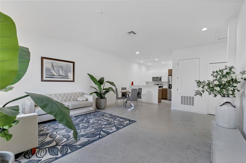 A bright open-concept living and dining area features white walls, tile floors, and modern furniture — 1563 CUMIN DRIVE, KISSIMMEE, FL