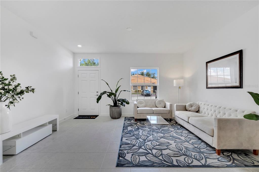 A bright living room features white walls, tile flooring, a patterned rug, and neutral furniture — 1563 CUMIN DRIVE, KISSIMMEE, FL