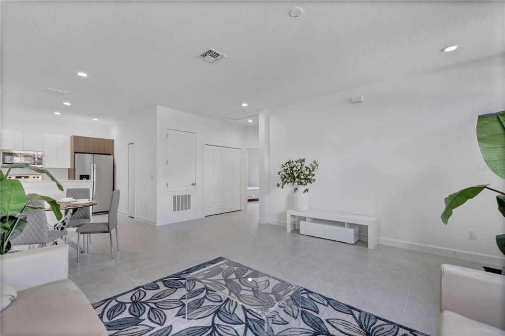 A bright, open-concept living room features white walls, light tile flooring, and a dining area — 1563 CUMIN DRIVE, KISSIMMEE, FL