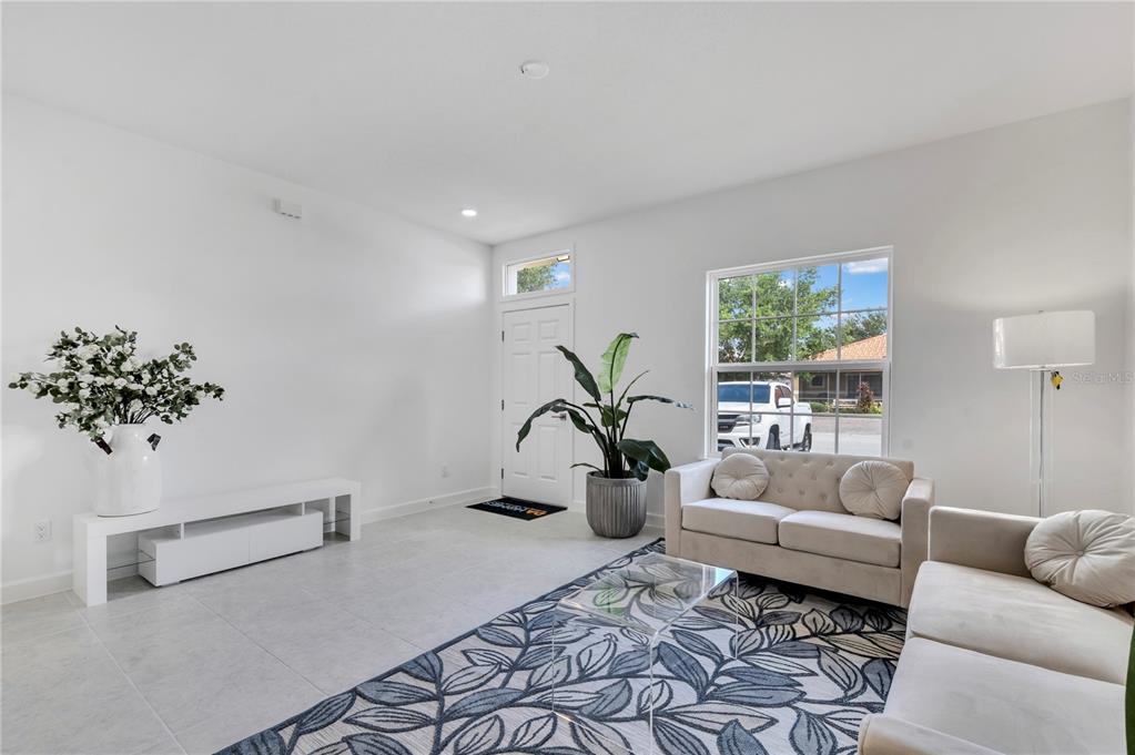 A bright living room features white walls, tile flooring, a patterned rug, and two sofas — 1563 CUMIN DRIVE, KISSIMMEE, FL