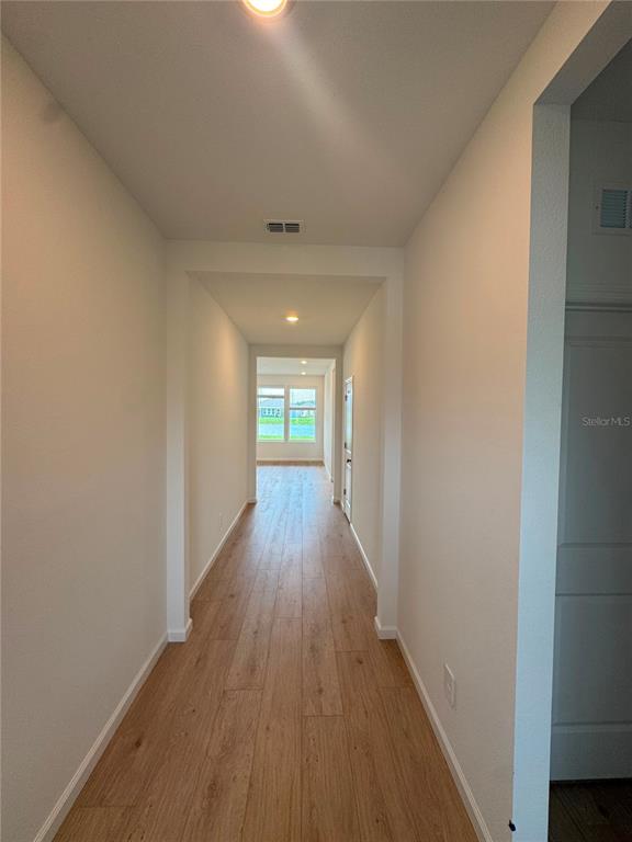 A long hallway with light wood-look flooring leads toward a window with a water view — 5543 MORANT BAY PATH, KISSIMMEE, FL