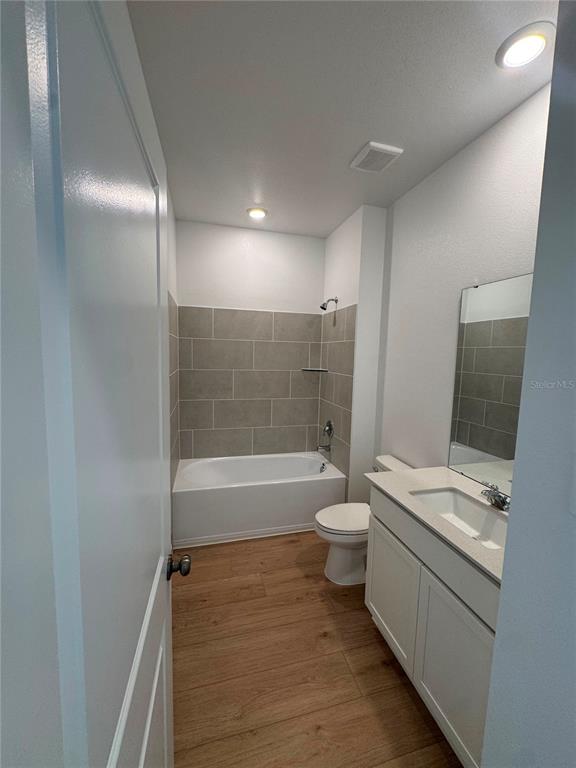 A bathroom features a tub-shower combo with gray tile, a vanity, and wood-look flooring — 5543 MORANT BAY PATH, KISSIMMEE, FL