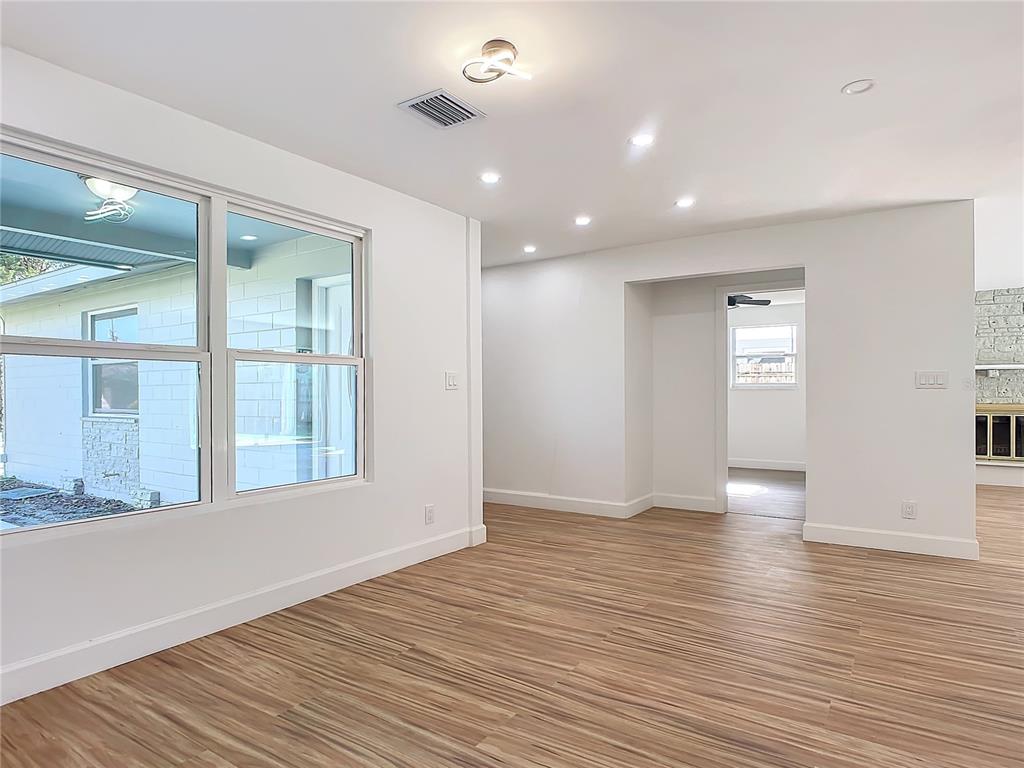 A bright, empty room features light wood-look flooring, white walls, recessed lighting, and large windows — 1428 MARGINA AVENUE, DAYTONA BEACH, FL