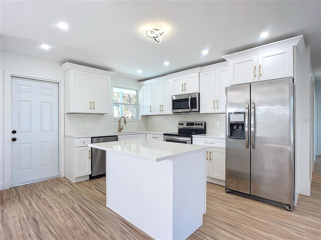 A white kitchen features a central island, stainless steel appliances, and light wood-look flooring — 1428 MARGINA AVENUE, DAYTONA BEACH, FL
