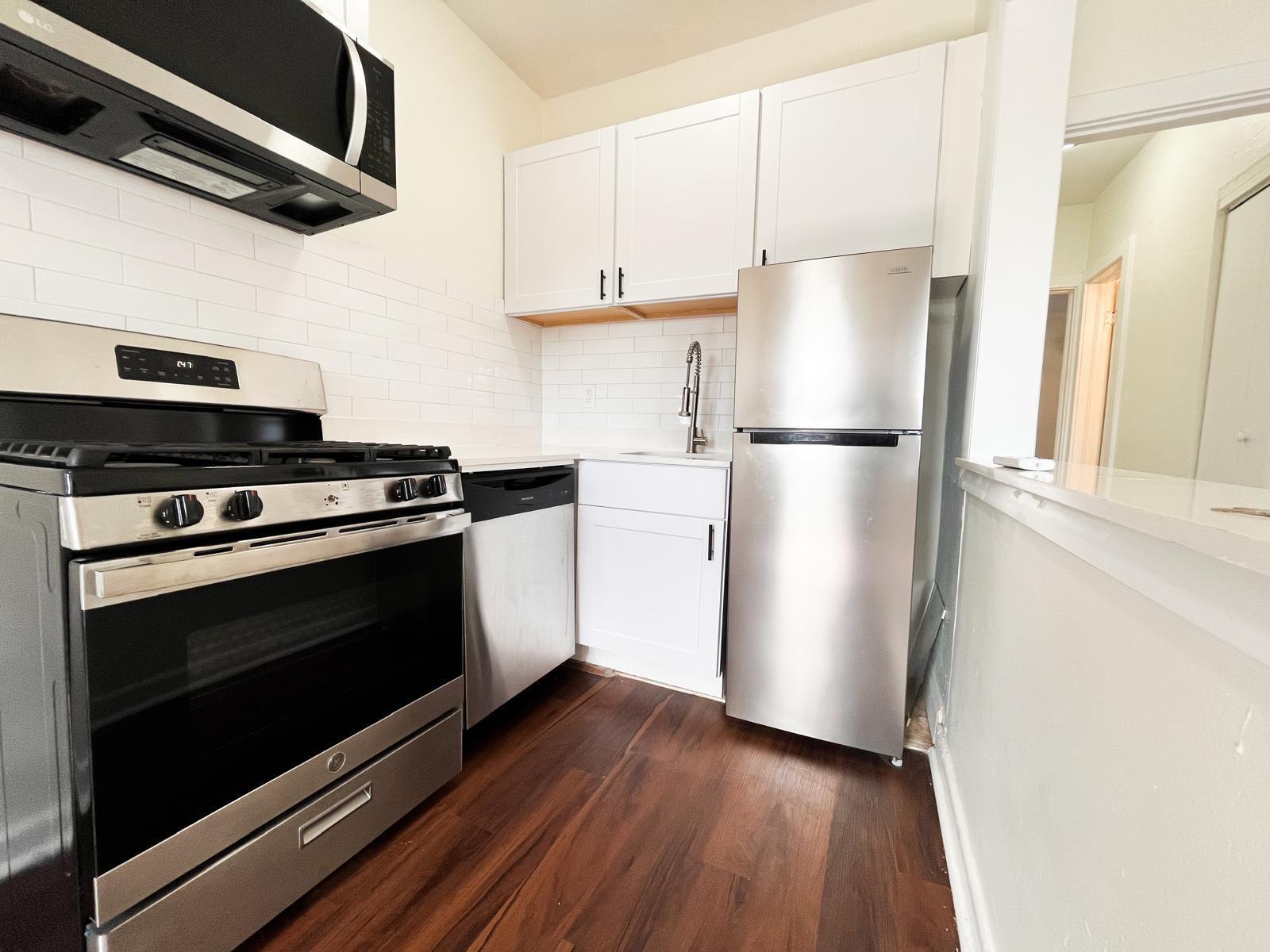 A small kitchen features stainless steel appliances, white cabinetry, subway tile backsplash, and wood flooring — 623 Park Place # 19, West Palm Beach FL 33401, WEST PALM BEACH, FL