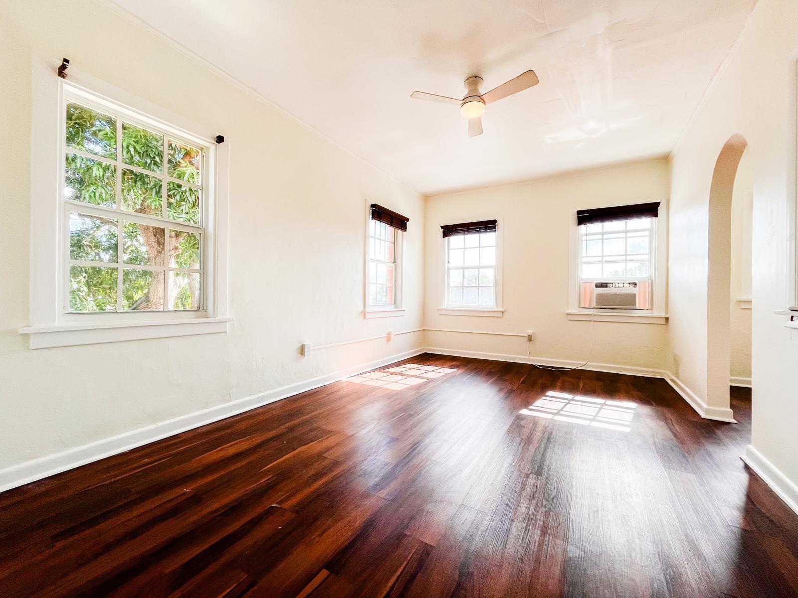 An empty room features dark wood floors, white walls, a ceiling fan, and multiple windows — 623 Park Place # 19, West Palm Beach FL 33401, WEST PALM BEACH, FL