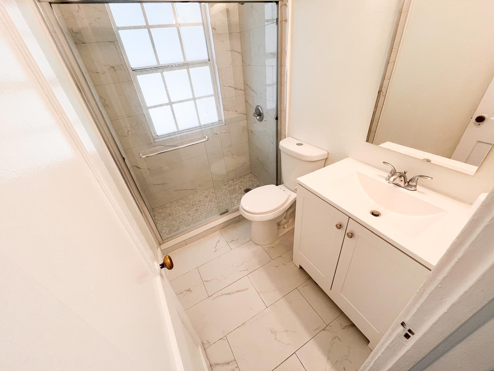 A small bathroom features a white vanity, a toilet, and a glass-enclosed walk-in shower — 623 Park Place # 19, West Palm Beach FL 33401, WEST PALM BEACH, FL