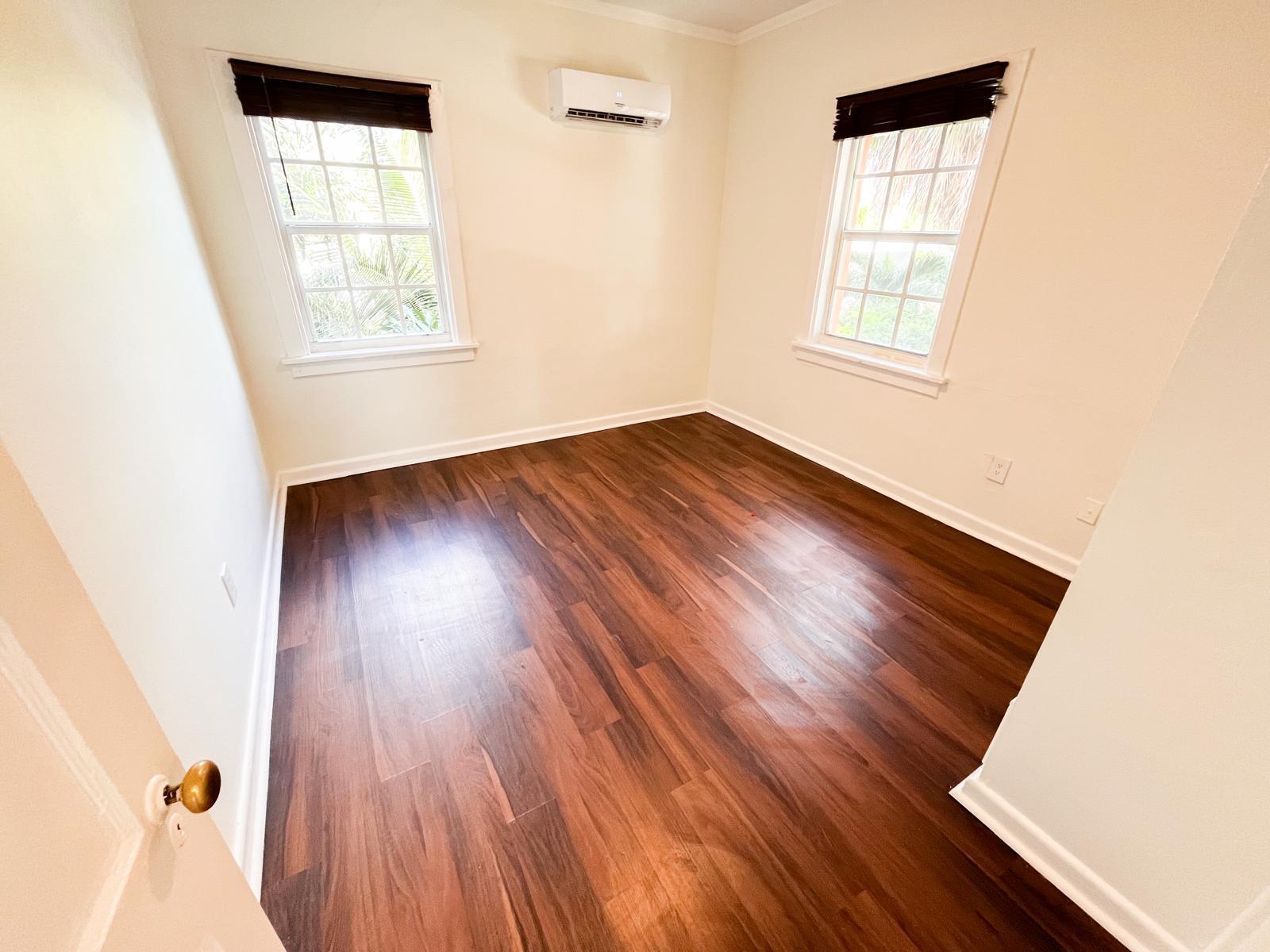 An empty bedroom with dark wood flooring, two windows, and a wall-mounted air conditioner — 623 Park Place # 19, West Palm Beach FL 33401, WEST PALM BEACH, FL
