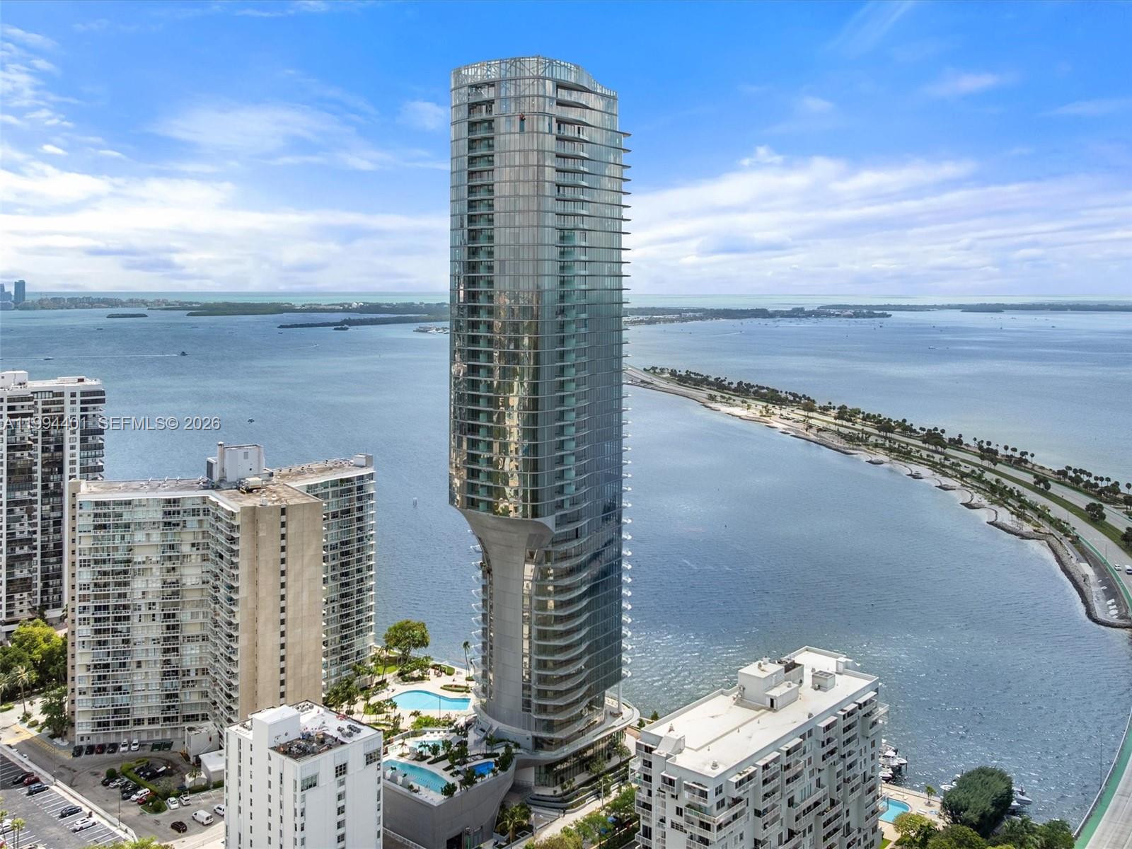 An aerial view shows a tall, modern glass skyscraper with a flared base near water — 175 SE 25th Rd # 502, Miami FL 33129, MIAMI, FL