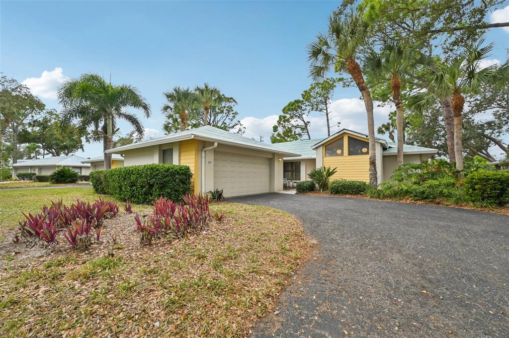 A single-story house with a yellow facade, a garage, and palm trees in the yard — 227 SOUTHAMPTON DRIVE UNIT 289, VENICE, FL