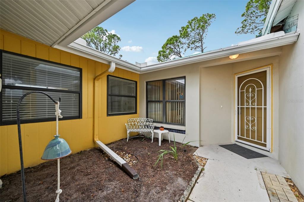 An exterior view of a home entrance with a small courtyard, yellow siding, and bench — 227 SOUTHAMPTON DRIVE UNIT 289, VENICE, FL