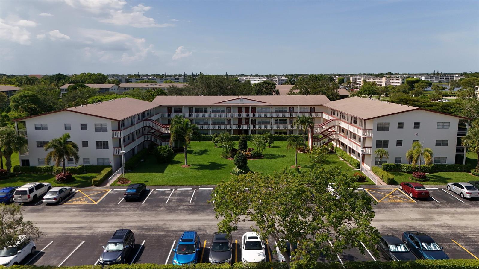 An aerial view of a multi-story apartment complex with a central courtyard and parking lot — 328 Brighton # H, Boca Raton FL 33434, BOCA RATON, FL