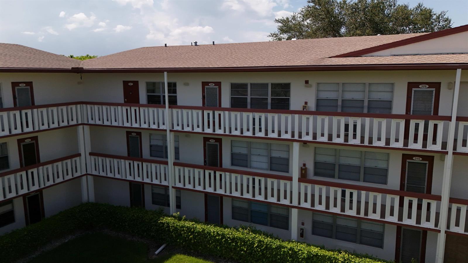An exterior view of a three-story apartment building with white balconies and red trim — 328 Brighton # H, Boca Raton FL 33434, BOCA RATON, FL