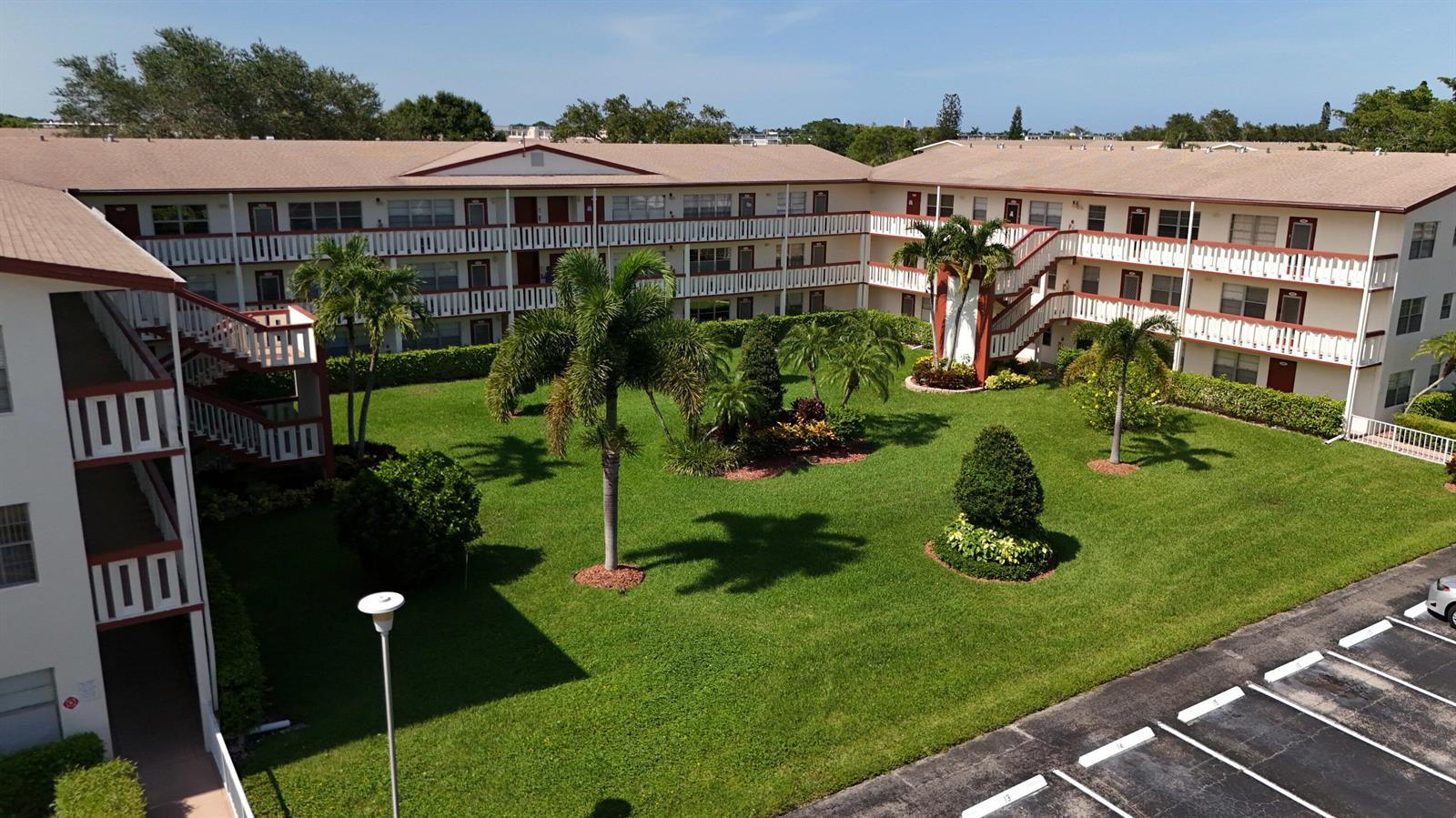 An aerial view of a multi-story apartment complex surrounding a grassy courtyard with palm trees — 328 Brighton # H, Boca Raton FL 33434, BOCA RATON, FL