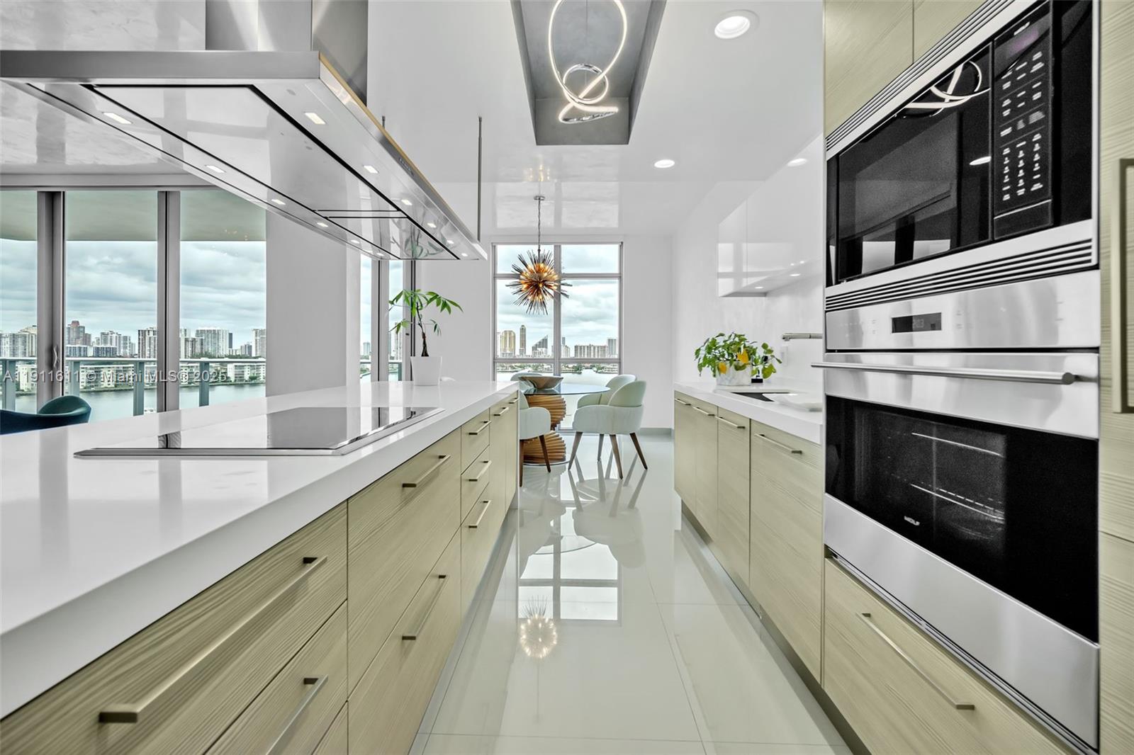 A modern kitchen features light wood cabinetry, white countertops, stainless steel appliances, and city views — 17301 Biscayne Blvd # 910, North Miami Beach FL 33160, NORTH MIAMI BEACH, FL