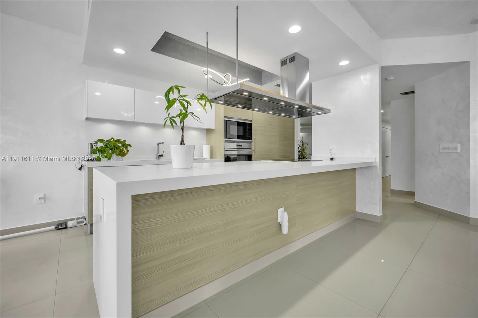 A modern kitchen features a white waterfall island, light wood cabinetry, and a stainless hood — 17301 Biscayne Blvd # 910, North Miami Beach FL 33160, NORTH MIAMI BEACH, FL