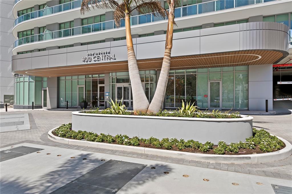 The exterior entrance of a modern residential building features a palm tree planter and signage — 400 CENTRAL AVENUE UNIT 3005, ST PETERSBURG, FL