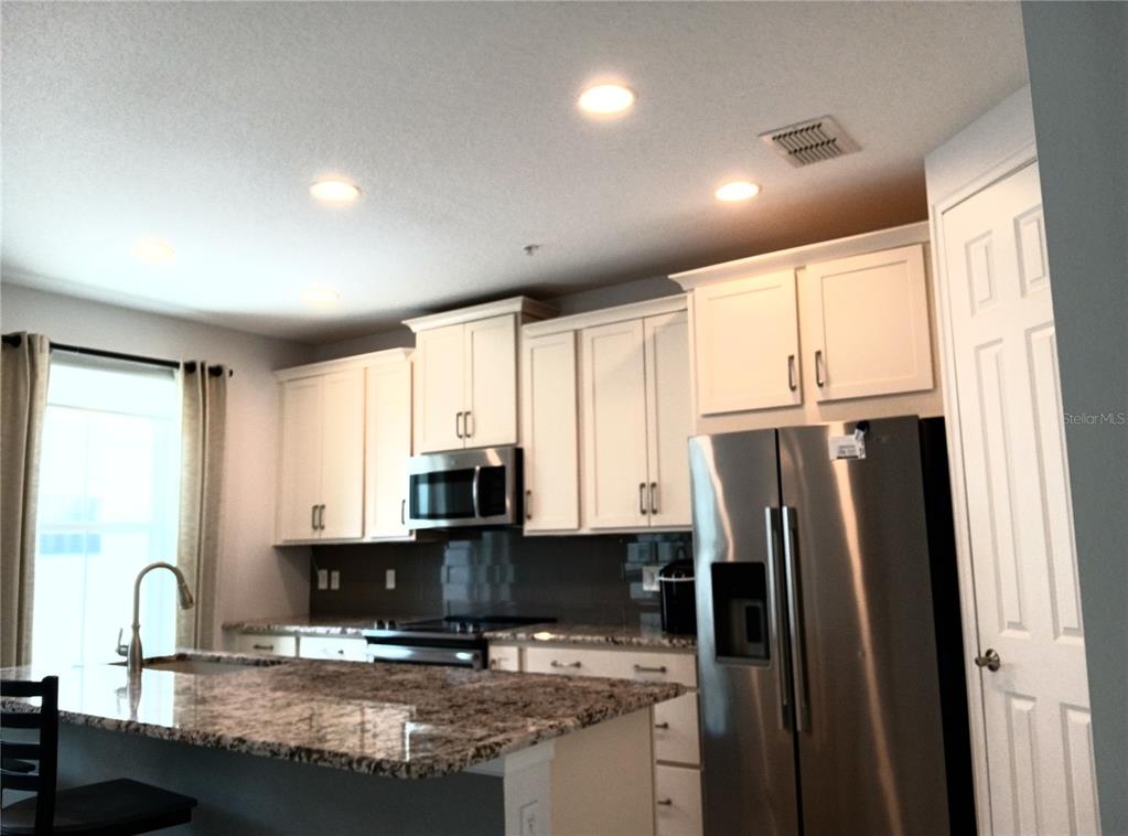 A kitchen with white cabinets, granite countertops, stainless steel appliances, and a center island — 933 BRUTUS TERRACE, LAKE MARY, FL