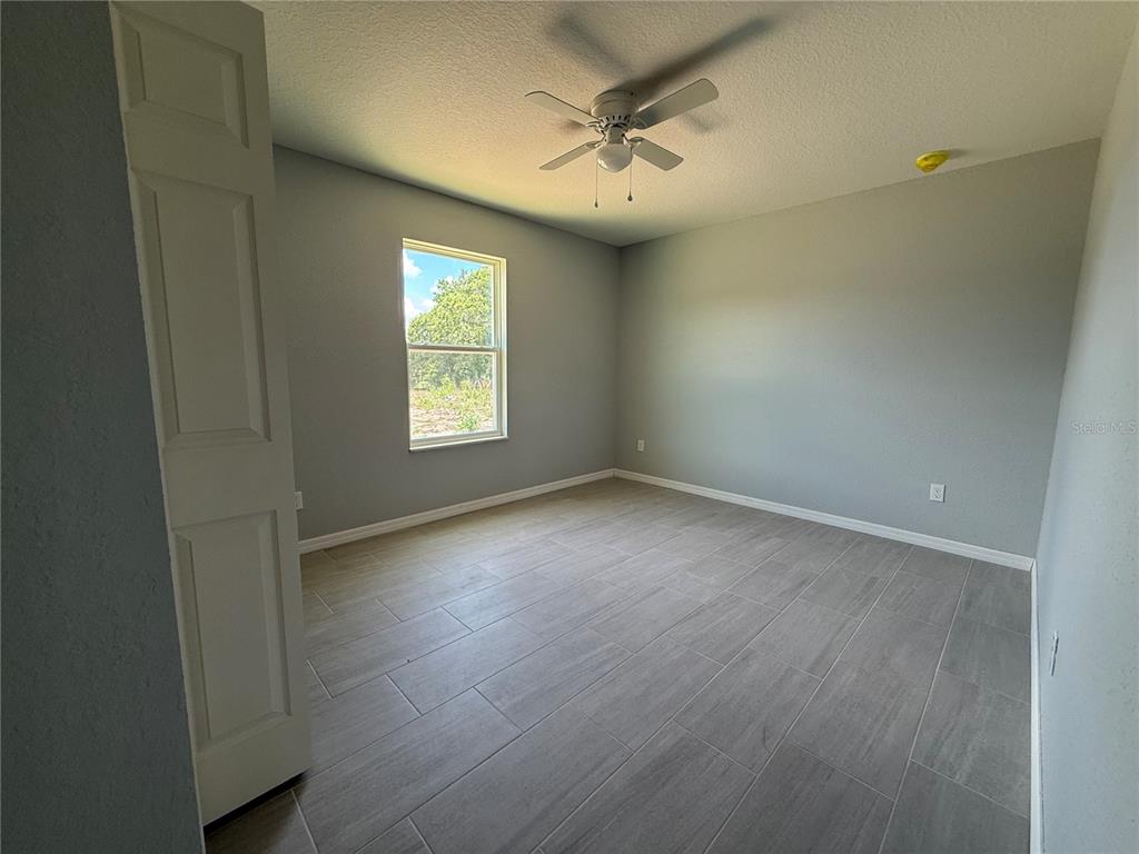 An empty bedroom features light gray walls, gray tile flooring, and a ceiling fan — 13108 SW 104TH LANE, DUNNELLON, FL