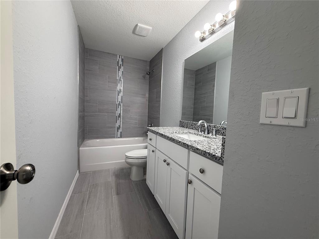 A bathroom features a white vanity with granite countertops, a tiled tub-shower, and gray flooring — 13108 SW 104TH LANE, DUNNELLON, FL