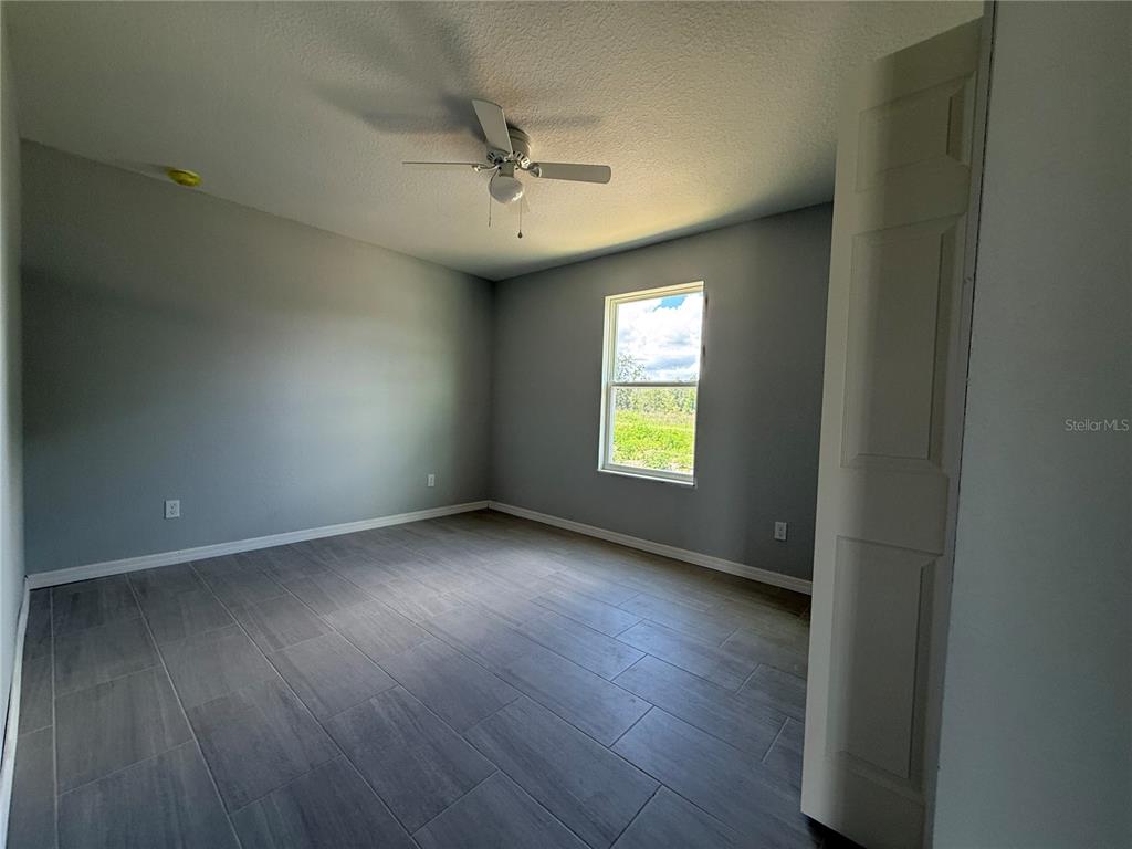 A bedroom with gray walls, wood-look tile flooring, a ceiling fan, and a single window — 13108 SW 104TH LANE, DUNNELLON, FL