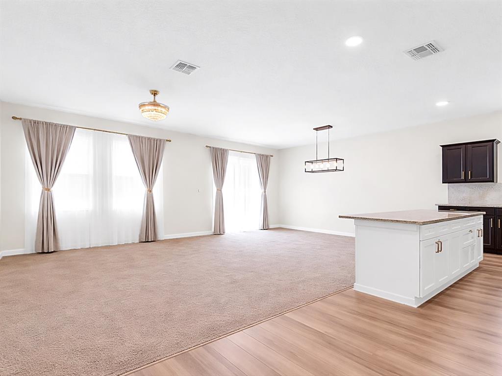 A spacious living area with carpeted flooring, large windows, and an adjacent kitchen island — 749 ORCHID GROVE BOULEVARD, DAVENPORT, FL