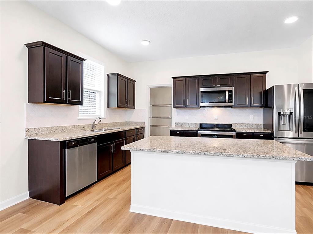 A kitchen features dark wood cabinets, granite countertops, stainless steel appliances, and light wood flooring — 749 ORCHID GROVE BOULEVARD, DAVENPORT, FL