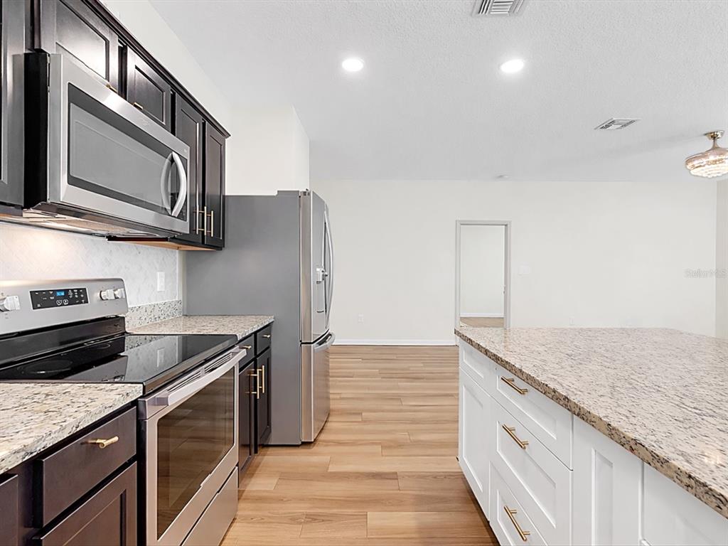 A kitchen features dark cabinets, stainless steel appliances, granite countertops, and a white island — 749 ORCHID GROVE BOULEVARD, DAVENPORT, FL