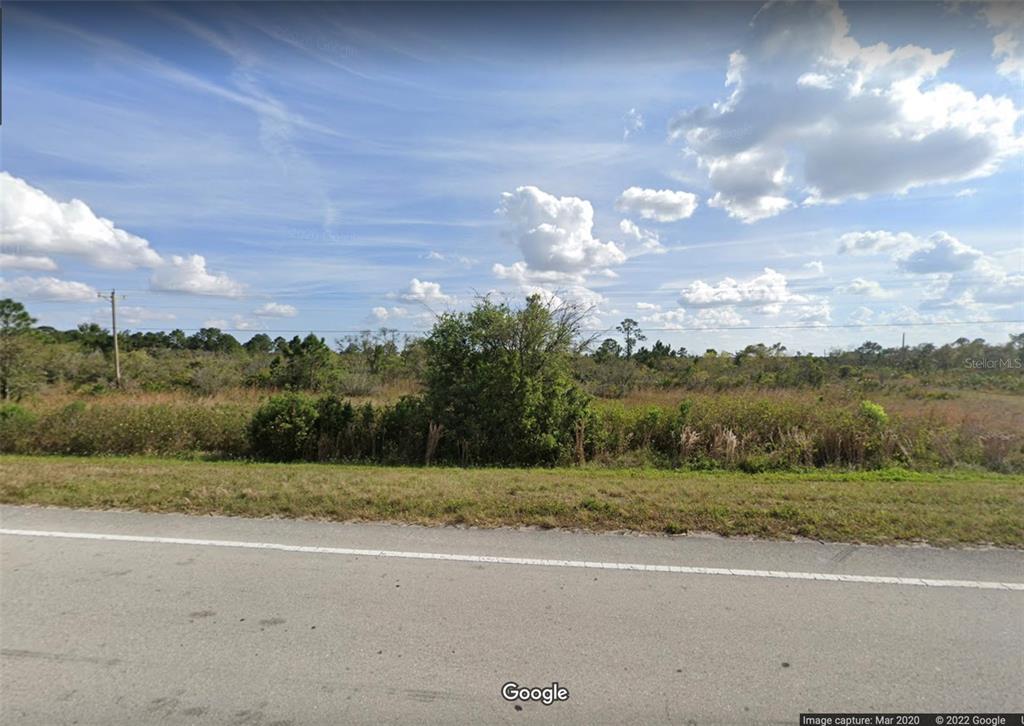 A view of a vacant, grassy lot with scattered shrubs and trees along a road — 475 STATE ROAD 70 E, LAKE PLACID, FL